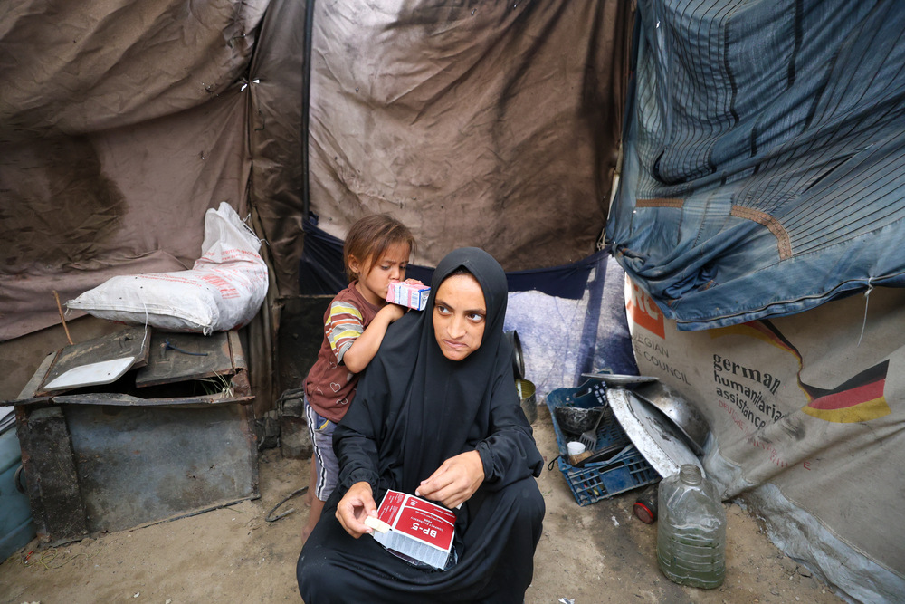 Nour jest w siódmym miesiącu ciąży. Je wysokoenergetyczne herbatniki na niedożywienie, obok jej córka pije mleko. Jej rodzina jest przesiedlona, żyje w namiocie i ma ograniczony dostęp do odżywczego jedzenia, co jest szczególnie groźne dla dzieci i kobiet w ciąży. Strefa Gazy, 2025